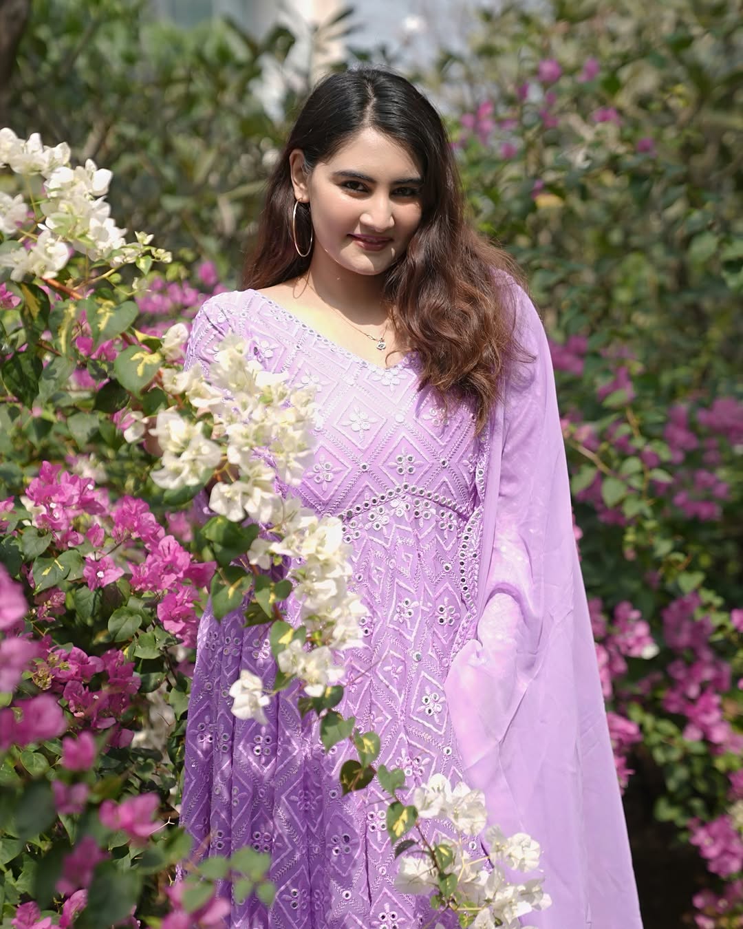 Woman in a purple saree standing among flowers