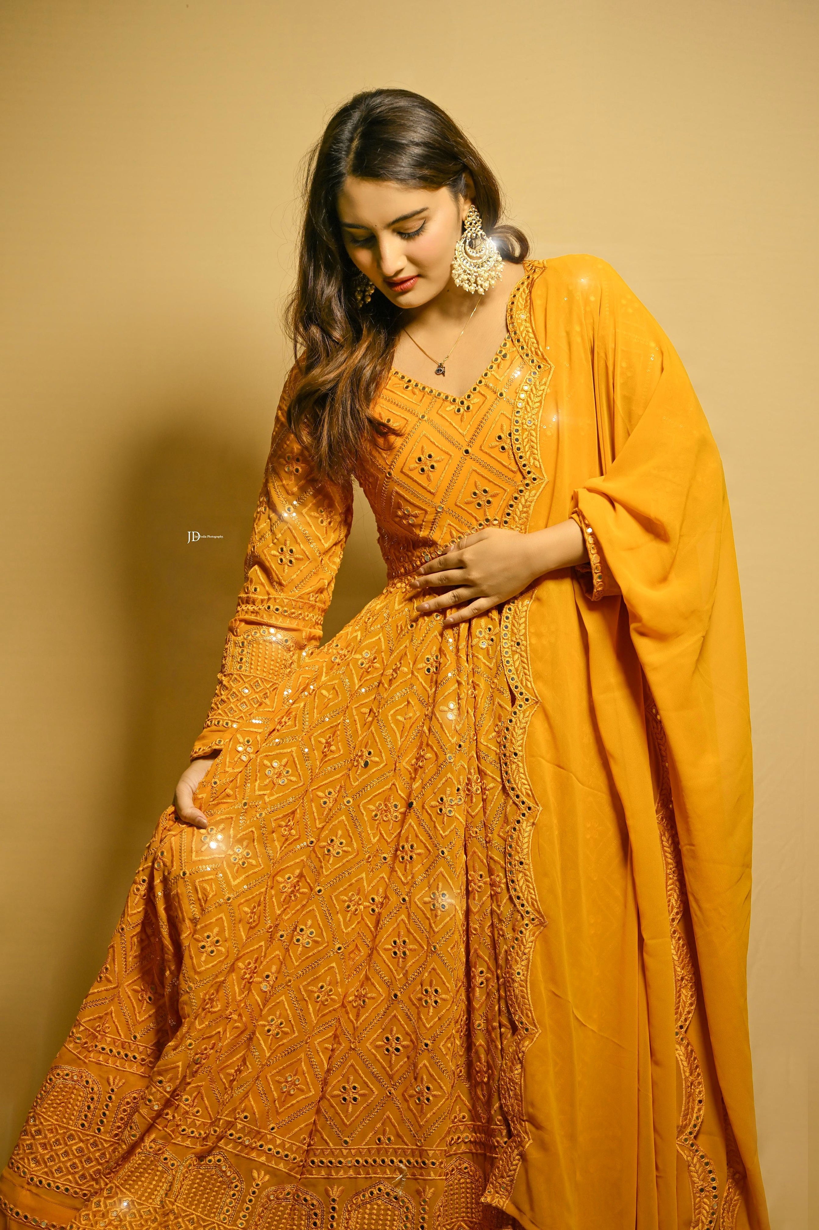 Woman wearing a mustard yellow traditional outfit with intricate patterns on a beige background