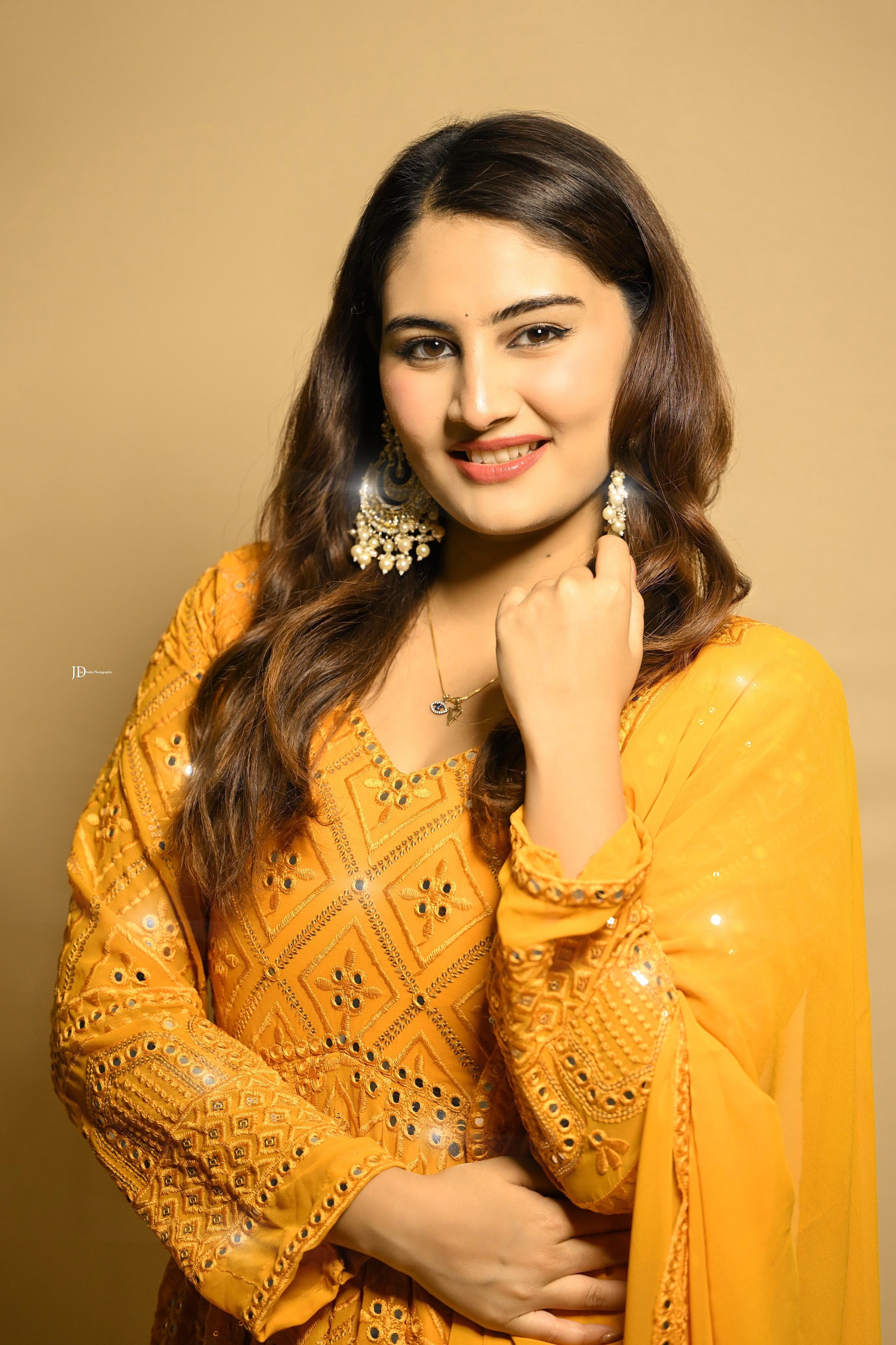 Woman wearing a yellow traditional outfit with intricate patterns on a beige background