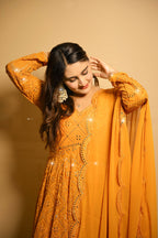 Woman wearing a mustard yellow traditional outfit with intricate designs on a beige background