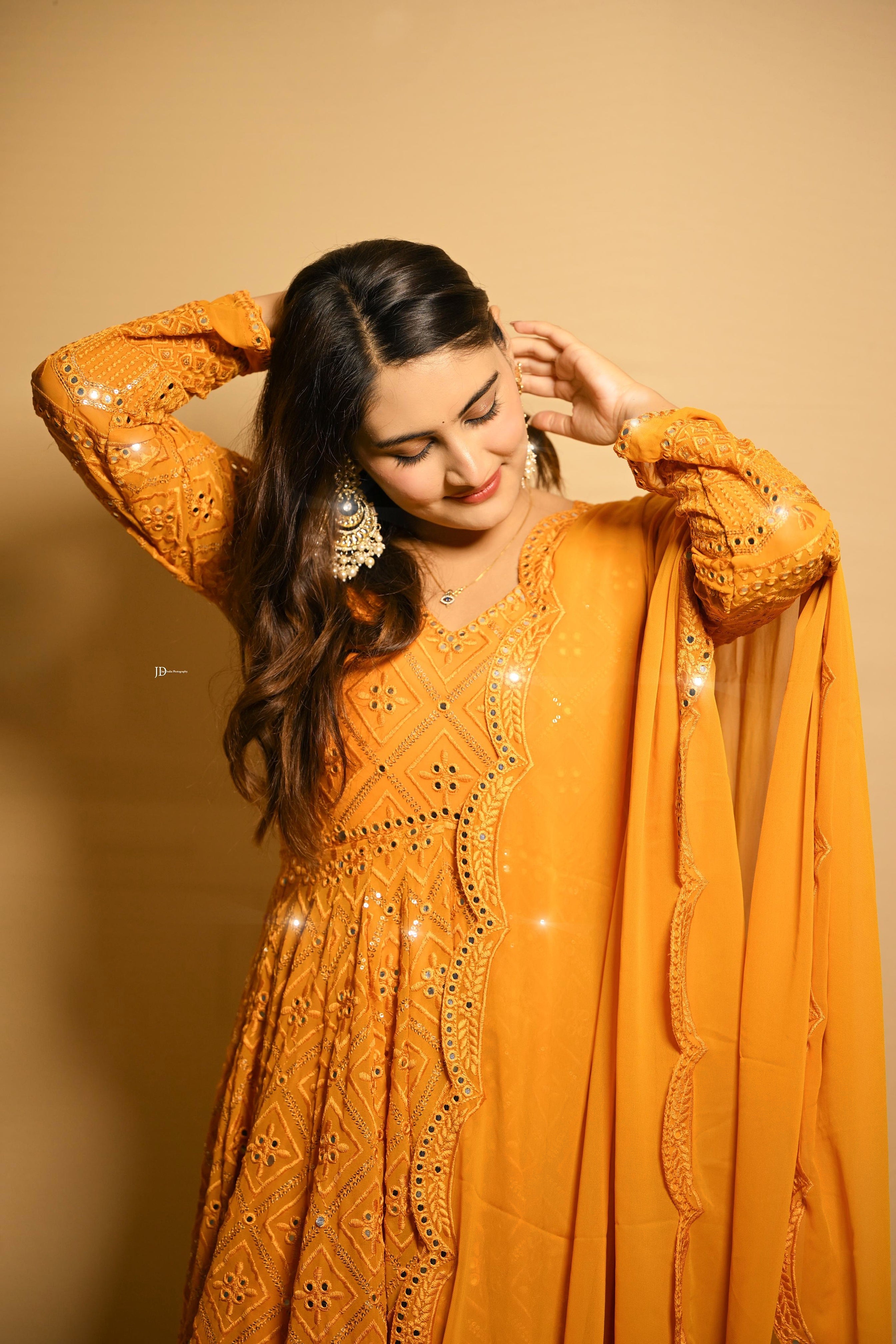 Woman wearing a mustard yellow traditional outfit with intricate designs on a beige background