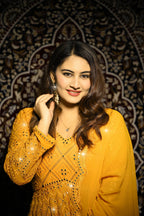 Woman in a yellow traditional outfit with intricate patterns against a decorative dark background