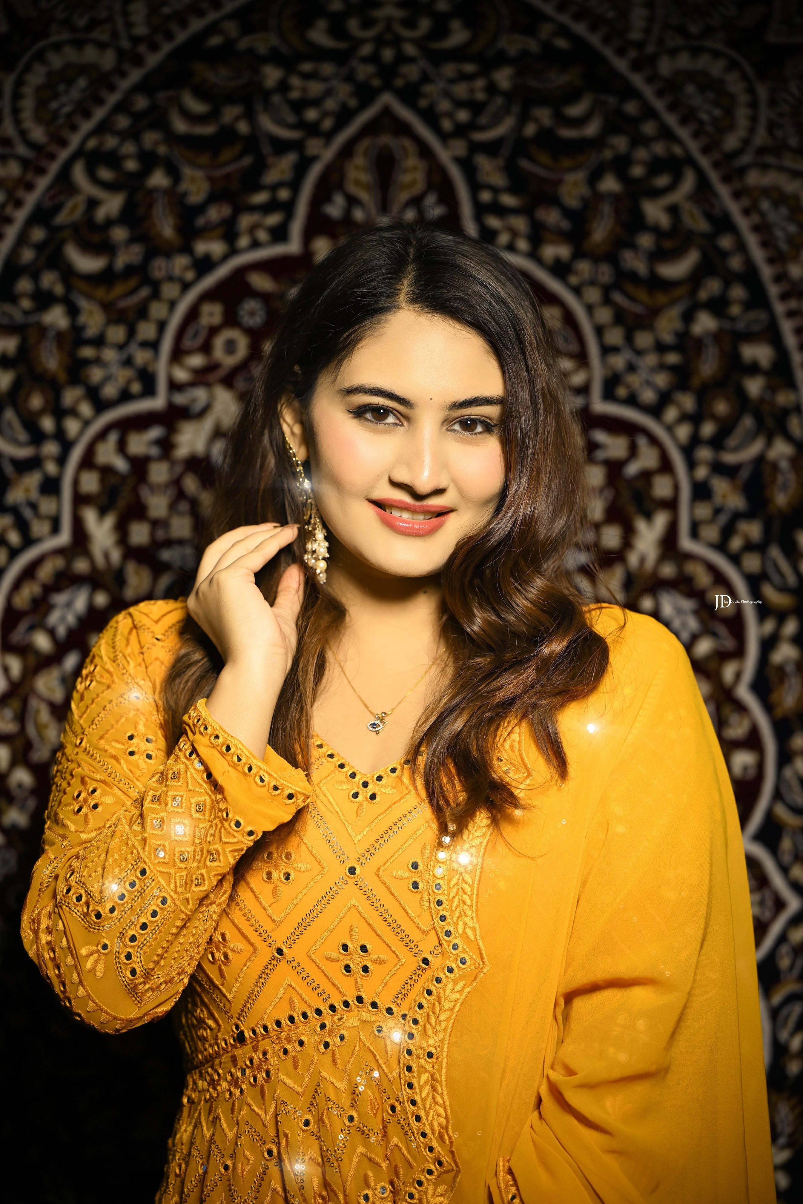 Woman in a yellow traditional outfit with intricate patterns against a decorative dark background